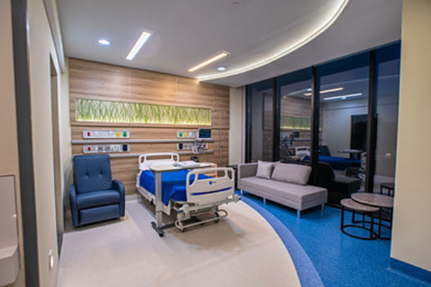 A hospital room with bed, couch, table and a single armchair.